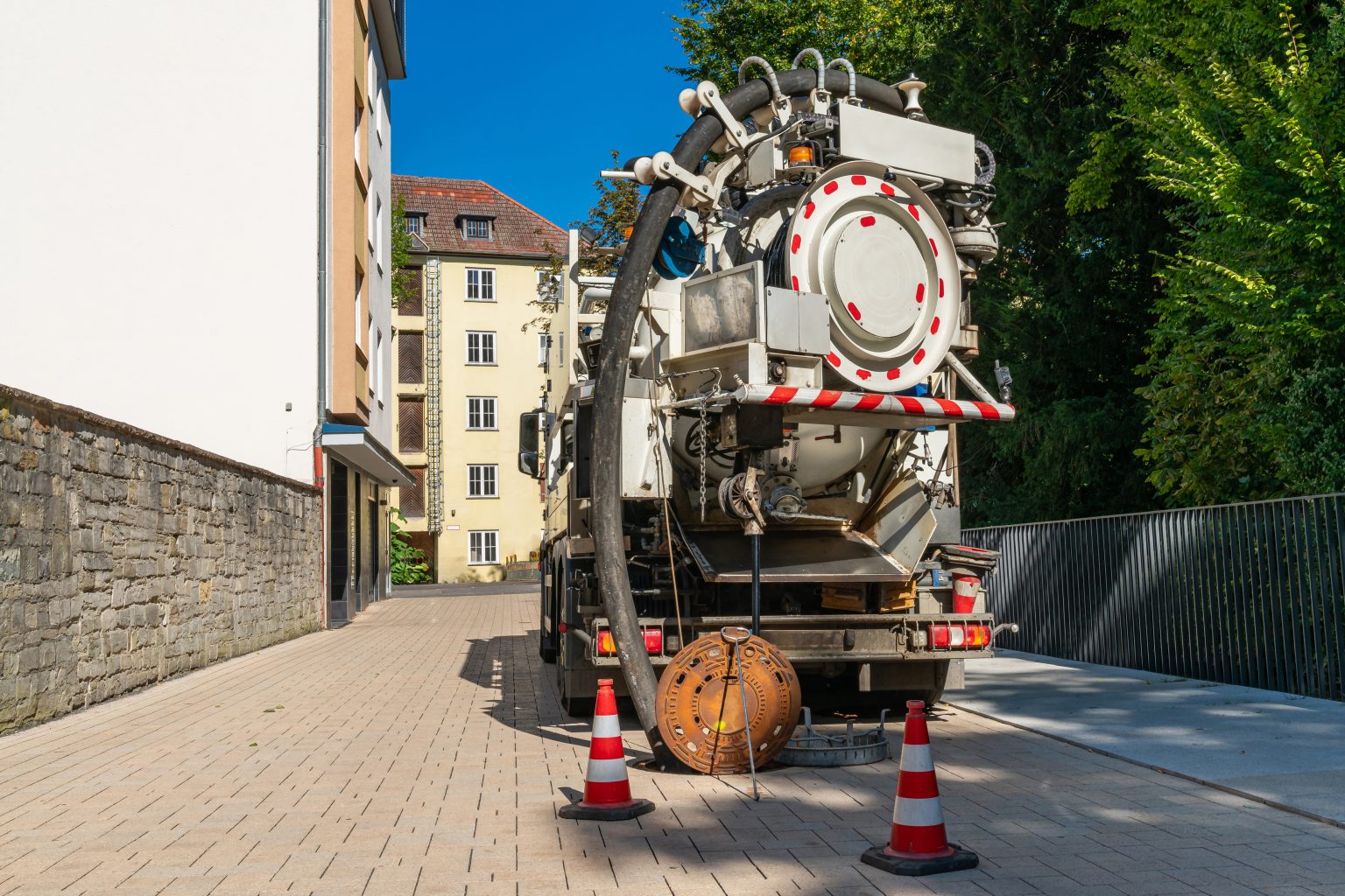 Sewage truck on the street with an open manhole .
