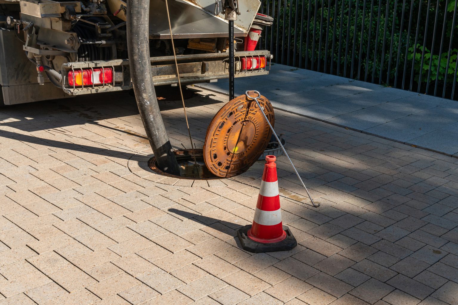 Open manhole on the street with a traffic cone and water hose.